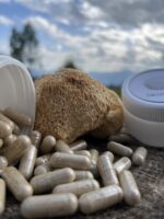 Капсули з порошком гриба їжовик гребінчастий поруч із цілим сушеним грибом, натуральна добавка на дерев’яній поверхні